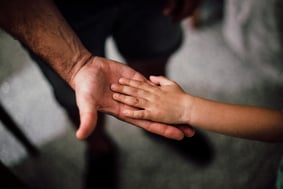 child's hand on top of adult's hand